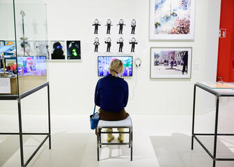 Eine Dame sitzt auf einer Bank und betrachtet einen Bildschirm der Ausstellung Public Matter(s) im Design Museum Gent.