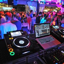 Bild von einer tanzenden Menschenmenge auf dem Vlasmarkt. Das Foto ist aus der Perspektive des DJs aufgenommen: Sie sehen die Plattenspiler im vordergrund und den Laptop in der Mitte.