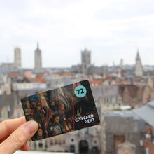 Hand met citycard Gent (72 u) met op de achtergrond de gekende skyline van Gent. (Vanop dak Gravensteen)