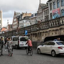 Witte taxi's staan te wachten naast de Sint-Michielsbrug. Voetgangers en fietsers passeren. 