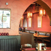 Muren geschilderd in oudroze met zwarte krullen, zitbanken, houten tafels en stoelen, groene lambrisering.