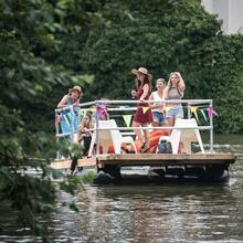 6 Personen fahren auf dem Fluss mit einem Floß mit Reling und Stühlen