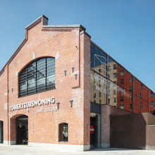 Groot industrieel gebouw, gerenoveerd, inkomdeuren met erboven de naam Direkteurswoning in witte letters.