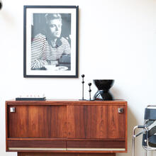 Een stijlvol mid-century dressoir van warm hout, gedecoreerd met vintage objecten en een bijpassende fotokader aan de muur